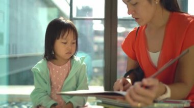 Asyalı Çinli Anne ve Kızı kütüphaneyi ziyaret ediyor ve kitapları karıştırıyor.