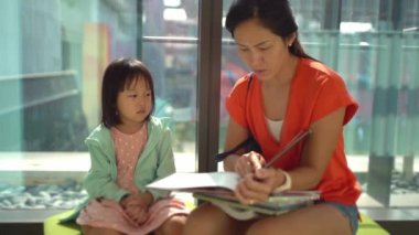 Asyalı Çinli Anne ve Kızı kütüphaneyi ziyaret ediyor ve kitapları karıştırıyor.