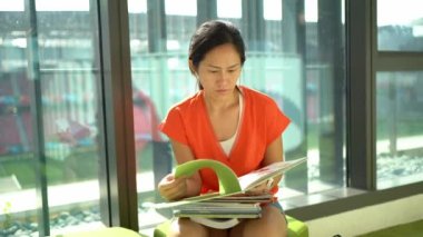 Asyalı Çinli kadın pencere kenarında oturup kitap okuyor ve çeviriyor.