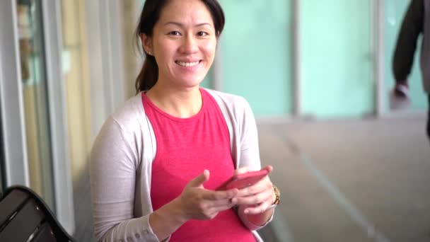 怀孕的亚裔母亲一边等着一边用智能手机抬头看 — 图库视频影像