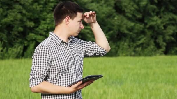 El caucásico macho morena agricultor en el campo trabaja con una tableta. Científico que trabaja en el campo con tecnología agrícola . — Vídeos de Stock