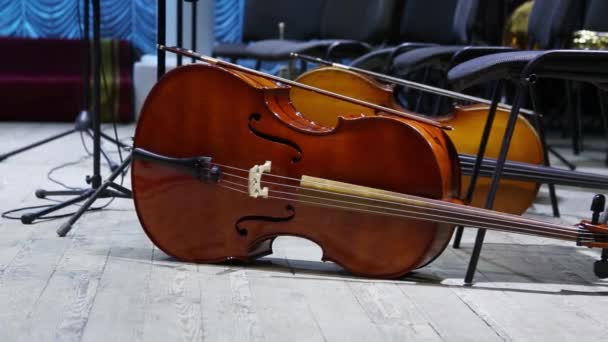 Cello i förgrunden och andra musikinstrument i bakgrunden ligger på golvet i scenen innan konserten — Stockvideo
