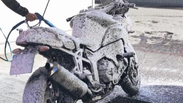 Um homem lava uma moto com espuma em uma máquina de lavar carros — Vídeo de Stock