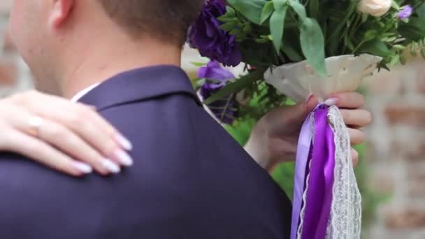 Couple de mariage étreignant, la mariée tenant un bouquet de fleurs dans sa main, le marié l'embrassant — Video