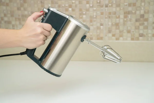 Mujeres mano sostiene mezclador eléctrico en una cocina moderna — Foto de Stock