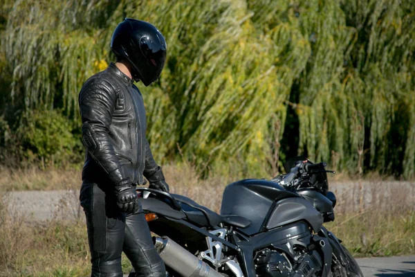 Bir motosiklet kask giymiş siyah motosikletçi görünüyor