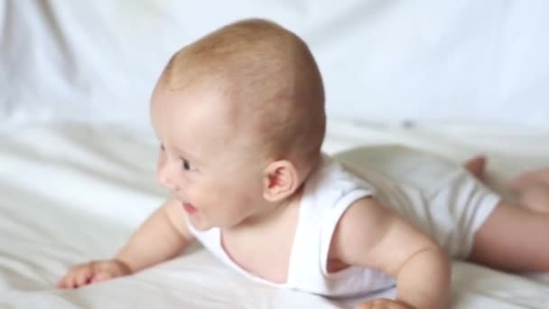 Aranyos boldog 6 hónapos kisfiú feküdt, és játszik egy fehér ágy — Stock videók