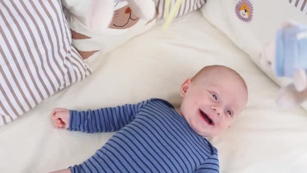 Lindo niño feliz de 6 meses mintiendo y jugando. Pequeño niño mirando sus juguetes — Vídeo de stock