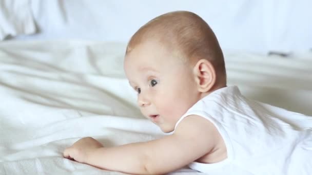 Aranyos boldog 6 hónapos kisfiú feküdt, és játszik egy fehér ágy