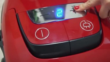Kadın kırmızı elektrik süpürgesini açıyor.