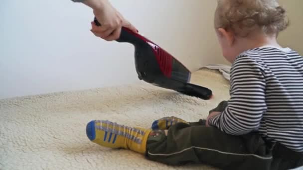 Малыш играет с пылесосом, пока мама не начнёт пылесосить — стоковое видео
