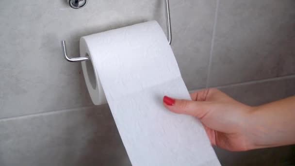 Молодая женщина берет в руки туалетную бумагу. Рука берет листы бумаги из рулона унитаза — стоковое видео
