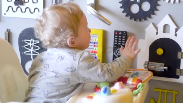 Bonito menino brincando com o tabuleiro ocupado na parede. Embarque ocupado para crianças. Placa de jogo de madeira — Vídeo de Stock