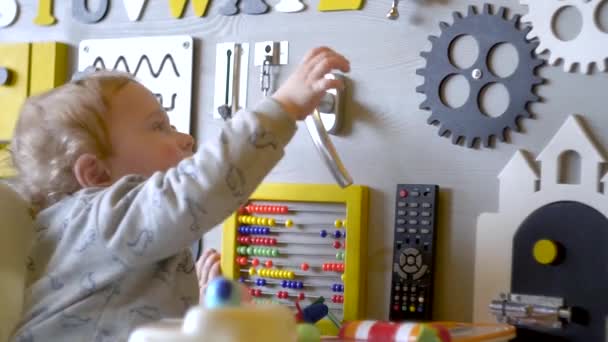 Милый мальчик играет с занятой доской на стене. Образовательные игрушки. Детская доска для занятий. Деревянная доска — стоковое видео
