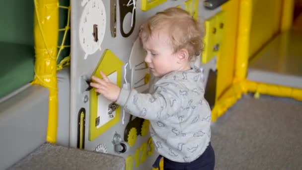 Niedlicher kleiner Junge, der mit beschäftigtem Brett an der Wand spielt. Lernspielzeug. Verpflegung für Kinder — Stockvideo