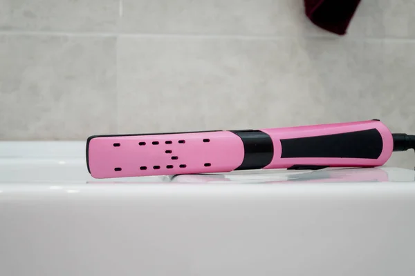 Endireitador de cabelo de rosa em um banheiro. Cuidados com o cabelo — Fotografia de Stock