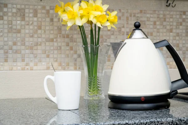 Bollitore di vetro elettrico con tazza e fiori gialli su una cucina domestica — Foto Stock