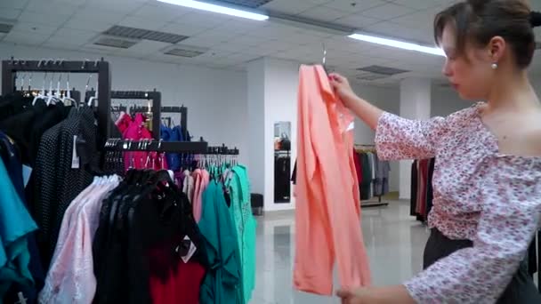 아름다운 소녀는 가게에서 셔츠를 선택했다. 쇼핑 소녀 — 비디오