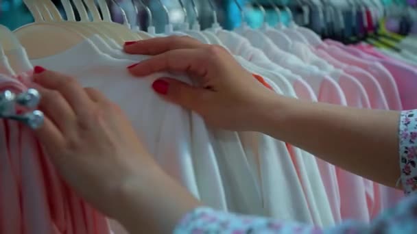 Μια νεαρή γυναίκα διάλεξε ένα μπλουζάκι στο μαγαζί. Κορίτσι για ψώνια — Αρχείο Βίντεο