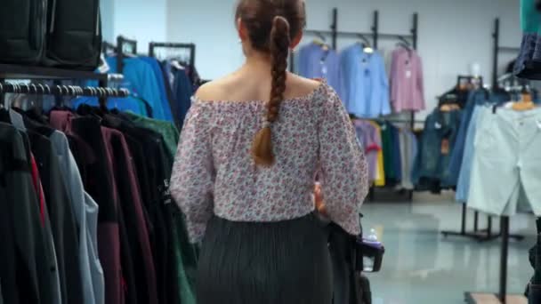 Mujer joven con un niño va a la tienda y elige la ropa — Vídeos de Stock