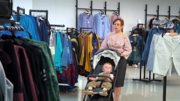 Όμορφο κορίτσι με ένα παιδί πηγαίνει στο κατάστημα και επιλέγει τα ρούχα — Αρχείο Βίντεο