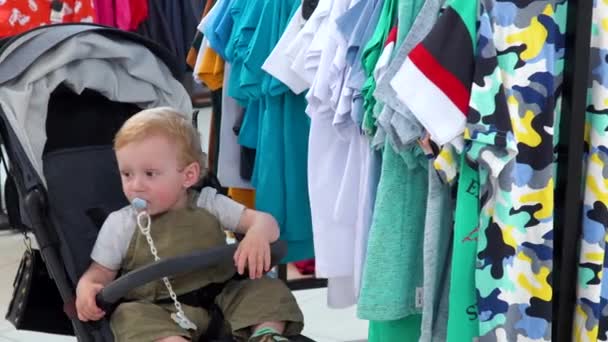 Schattige kleine jongen zitten in baby buggy in een kledingwinkel — Stockvideo