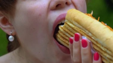 Bir şehir parkında zevkle sosisli yiyen kız. Yavaş çekim