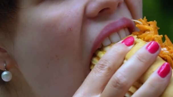 Fiatal nő eszik hot dog örömmel egy városi parkban — Stock videók