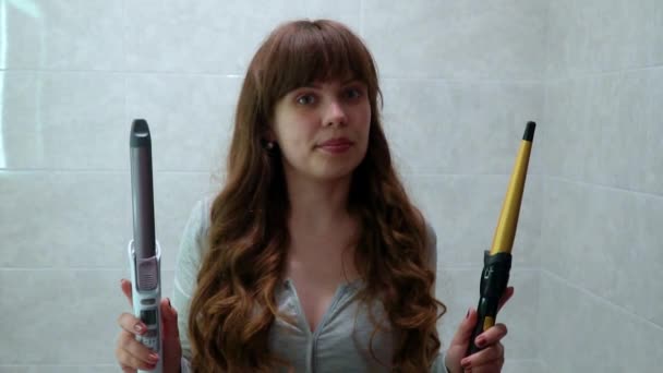 Woman holds two hair straighteners in the bathroom. Girl chooses hair straightener. Slow motion — Stock Video