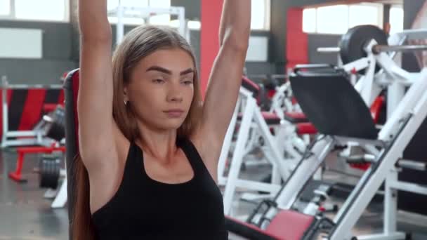 Joven mujer de fitness haciendo ejercicio en el gimnasio con pesas sentadas en el banco — Vídeo de stock