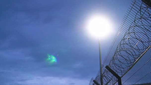 Grande clôture de prison avec fil barbelé la nuit éclairée par une lanterne — Video