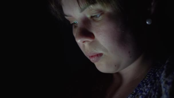 Vrouw met behulp van mobiele telefoon in het donker en glimlacht — Stockvideo