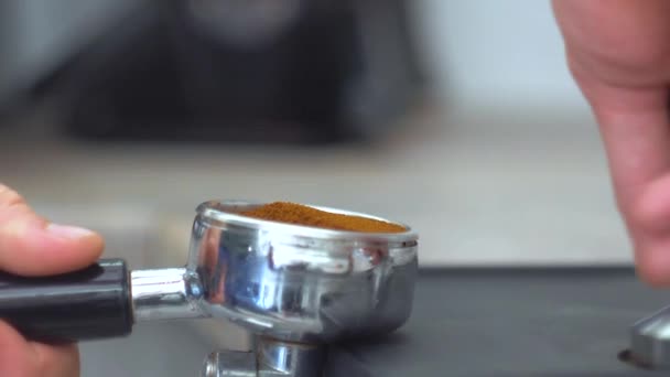 Un primer plano de una mano sosteniendo un portafilter con café molido en el borde de la mesa. Haciendo café — Vídeos de Stock