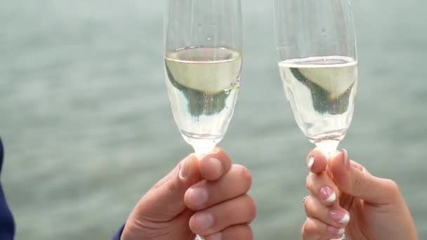 Homem e mulher batendo copos de champanhe espumante contra fundo de água corrente. Fechar de copos e mãos — Vídeo de Stock