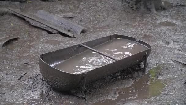 Un viejo bebedero lleno de agua en el medio del patio trasero. Suelo húmedo bajo la lluvia. Charcos y pantanos — Vídeos de Stock