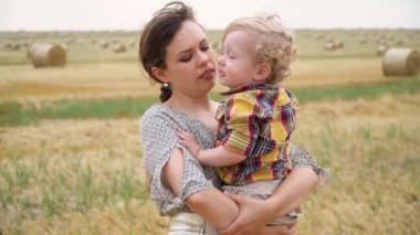 Güzel genç kadın, yaz akşamı balyalarla buğday tarlasının ortasında kollarında güzel saçlı küçük bir oğlu var. Anne oğlunu öpüyor