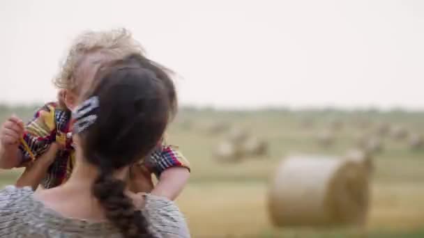 Красива молода жінка з симпатичним маленьким сином на руках посеред пшеничного поля з тюками в літній вечір — стокове відео