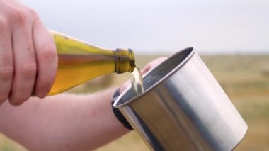 Bir adam balyalarla buğday tarlasındaki metal bir bardağa bira döküyor.