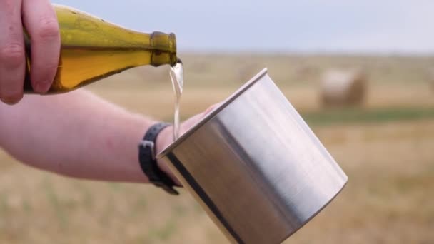 Muž nalije pivo do kovové skleničky na pšeničném poli s balany. — Stock video