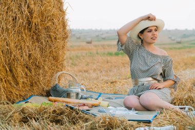 Güzel kız yaz akşamı bir buğday tarlasının ortasında bir saman balyası yakınında piknik yapıyor