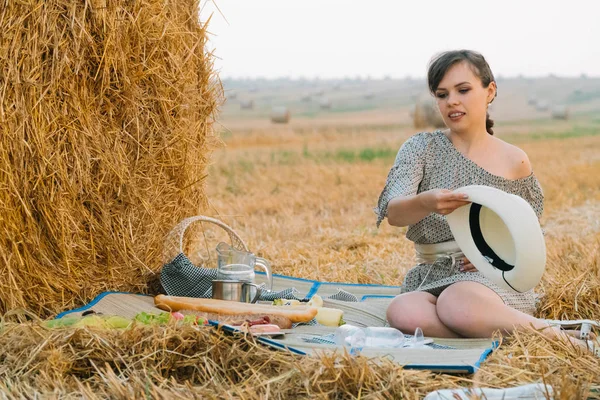 Güzel kız yaz akşamı bir buğday tarlasının ortasında bir saman balyası yakınında piknik yapıyor