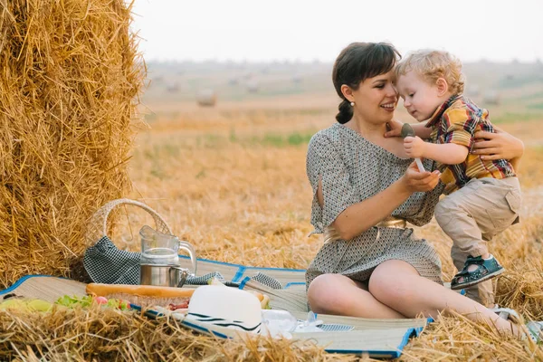Yaz akşamı buğday tarlasının ortasında saman balyası yakınında piknik küçük sarışın oğlu ile güzel genç kadın