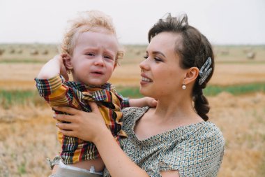 Yaz akşamı balyalar ile bir buğday tarlasının ortasında kollarında sarışın küçük ağlayan oğlu ile güzel genç kadın