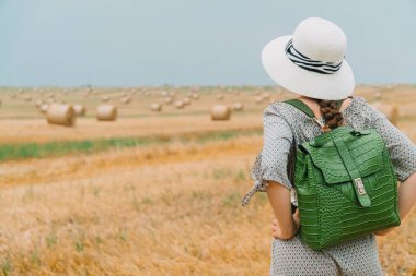 Şapkalı güzel bir kız ve bir yaz akşamında balyalarla dolu bir buğday tarlasının ortasında sırt çantasıyla