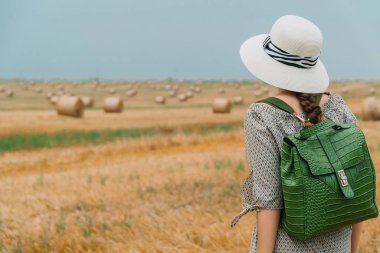 Şapkalı, sırt çantalı, buğday tarlasının ortasında balyaları olan güzel bir kadın.