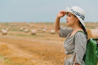 Şapkalı güzel bir kız ve bir yaz akşamında balyalarla dolu bir buğday tarlasının ortasında sırt çantasıyla