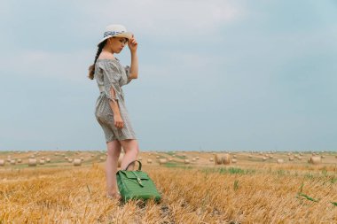 Şapkalı, sırt çantalı, buğday tarlasının ortasında balyaları olan güzel bir kadın.