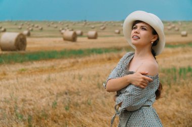 Şapkalı güzel kız, yaz akşamları balyalarıyla bir buğday tarlasının ortasında gökyüzüne bakıyor.