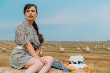 Güzel genç kadın yaz akşamı balya ile buğday tarlasının ortasında balya üstünde oturan