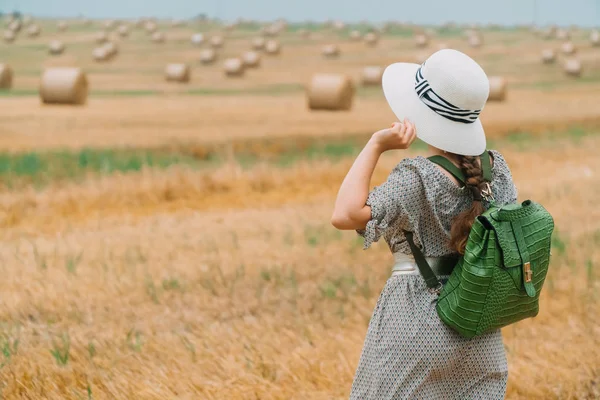 Şapkalı güzel bir kız ve bir yaz akşamında balyalarla dolu bir buğday tarlasının ortasında sırt çantasıyla